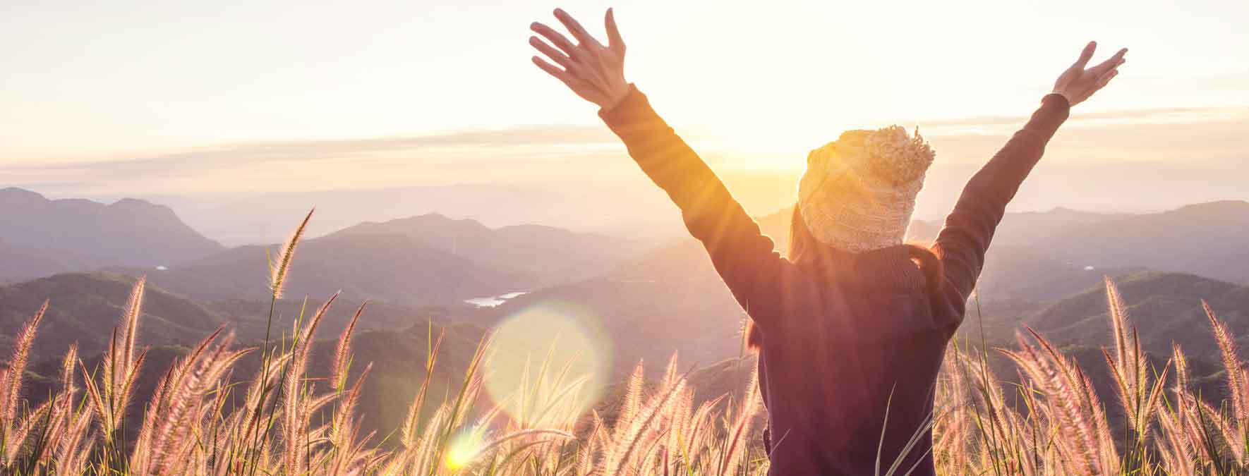 Ein Frau streckt Arme und Hände in die Luft und schaut dem Sonnenuntergang zu